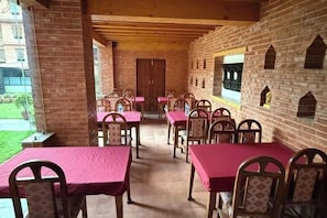 Un espace extérieur abrité, aménagé pour les repas, avec des murs en briques, des tables et des chaises en bois.