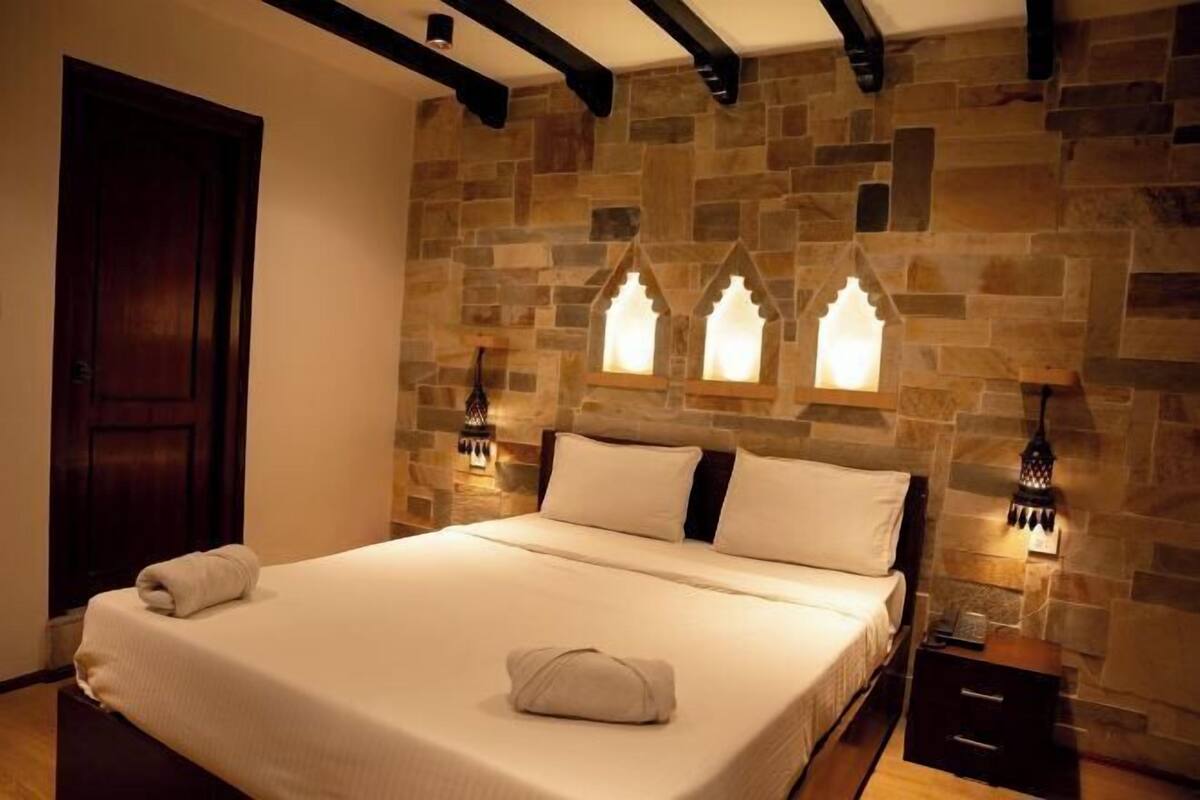 Una camera da letto con una parete in pietra, un letto con lenzuola bianche e due luci fissate al muro.
