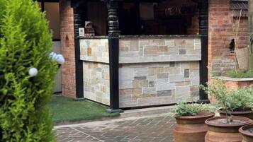 Een bar met stenen blad, een achtergrond van bakstenen muur, potplanten en een verzorgd gazon.