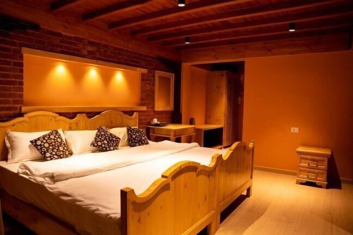 Un letto di legno con testiera, un comodino e un tavolino da notte in una stanza con pareti in mattoni e travi a vista.