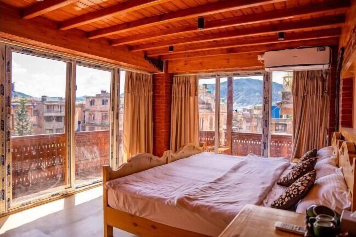 Una stanza con struttura in legno, un letto, ampie finestre e un condizionatore d'aria.