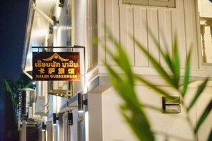 A sign for Nalinn Guesthouse with Thai text, a white building facade, and a plant in the foreground. - Nalin Guesthouse(casa) (Luang Prabang)