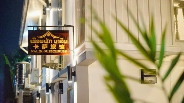 A sign for Nalinn Guesthouse with Thai text and a logo.
