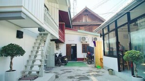 A narrow alleyway with a staircase leading to a building with a wooden facade. There are potted plants and a motorcycle parked outside.