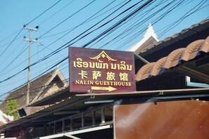 Schild für das Nalinn Guesthouse vor traditioneller thailändischer Architektur.