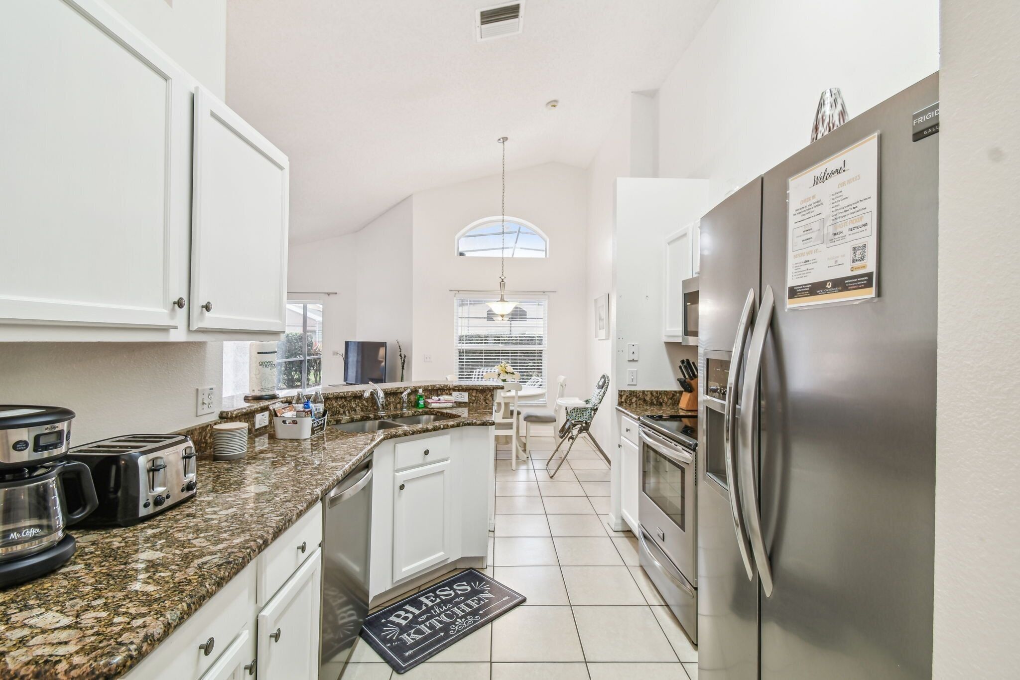 A modern kitchen with white cabinets, granite countertops, a stainless steel refrigerator, and a dining area with a table and chairs.