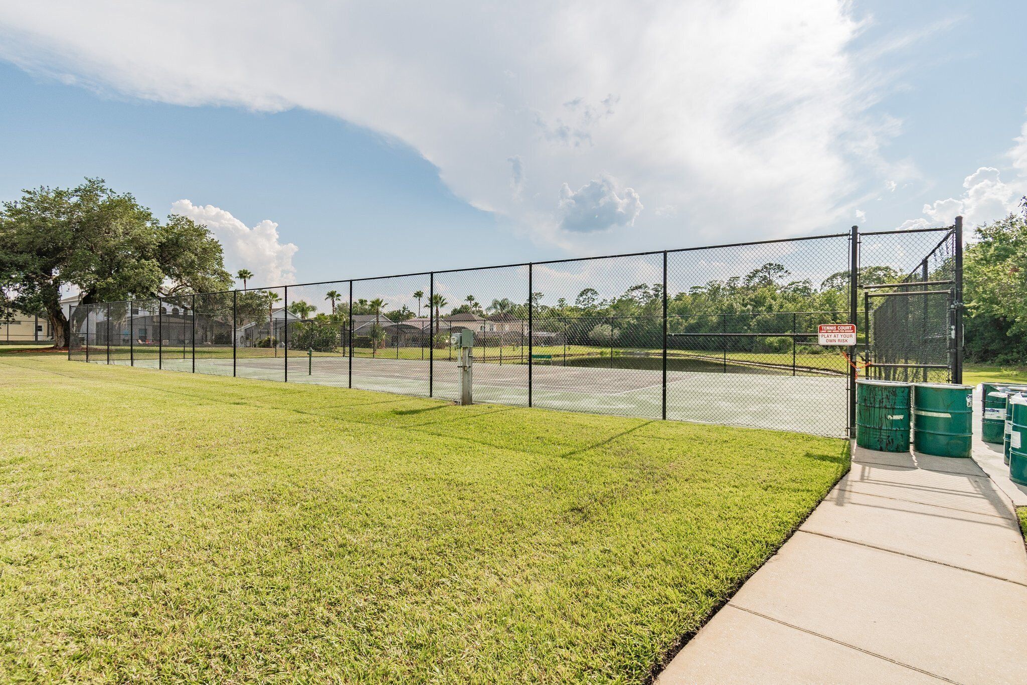 A fenced tennis court with a clear sky and a grassy area in the foreground.