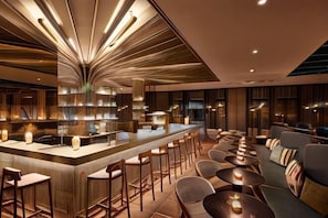 Zona de bar con barra curva, varios taburetes y una sala de estar con mesas redondas y sofás.