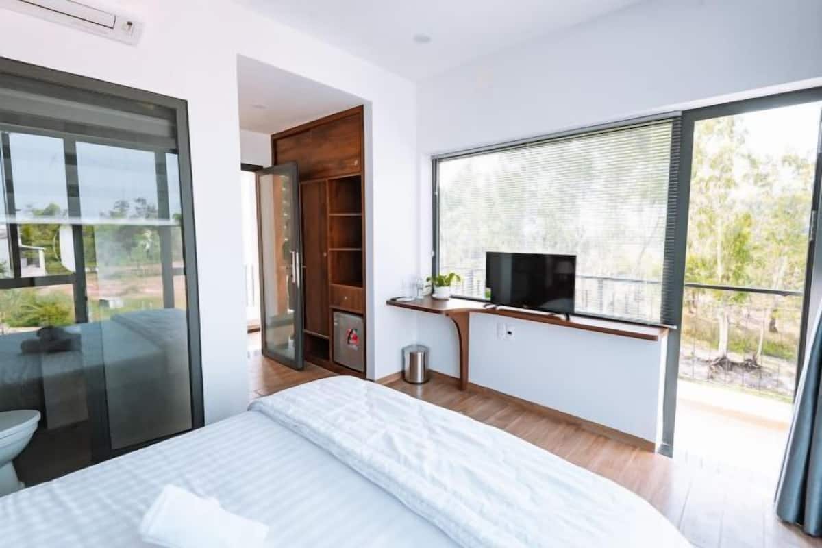 Une chambre moderne équipée d’un lit, d’une télévision, d’un bureau et d’une porte coulissante donnant sur un balcon.