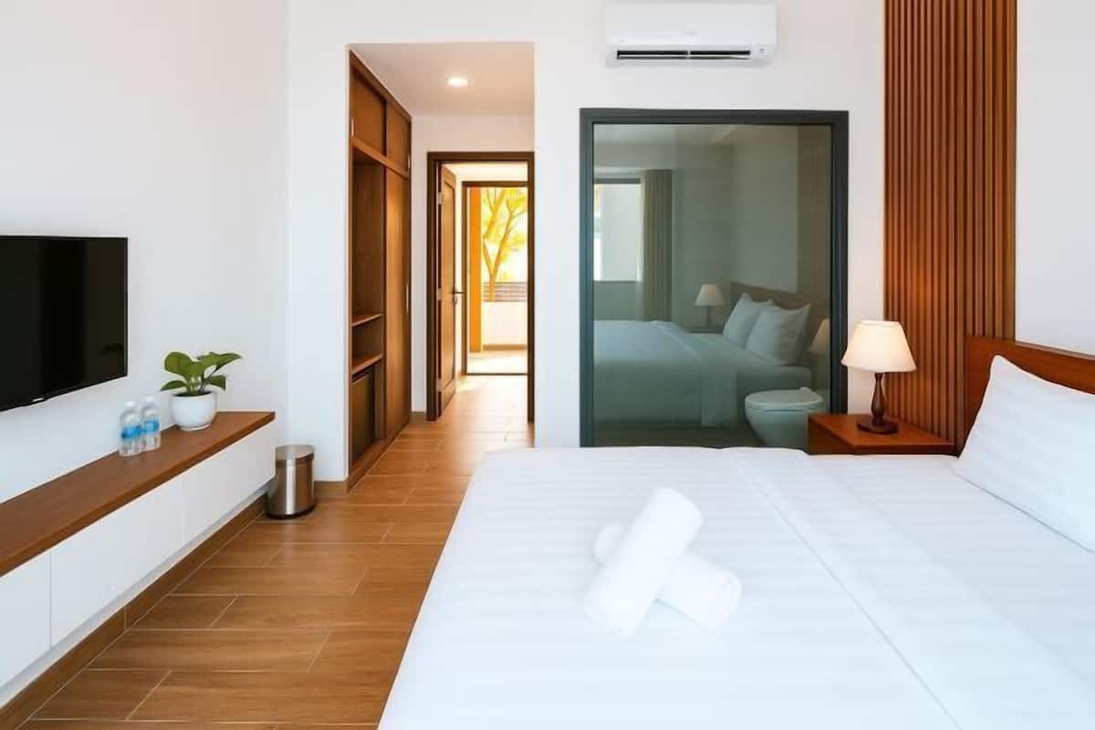 Une chambre d’hôtel avec un lit, une lampe de chevet, une télévision, une plante en pot et une vue à travers une porte vitrée.