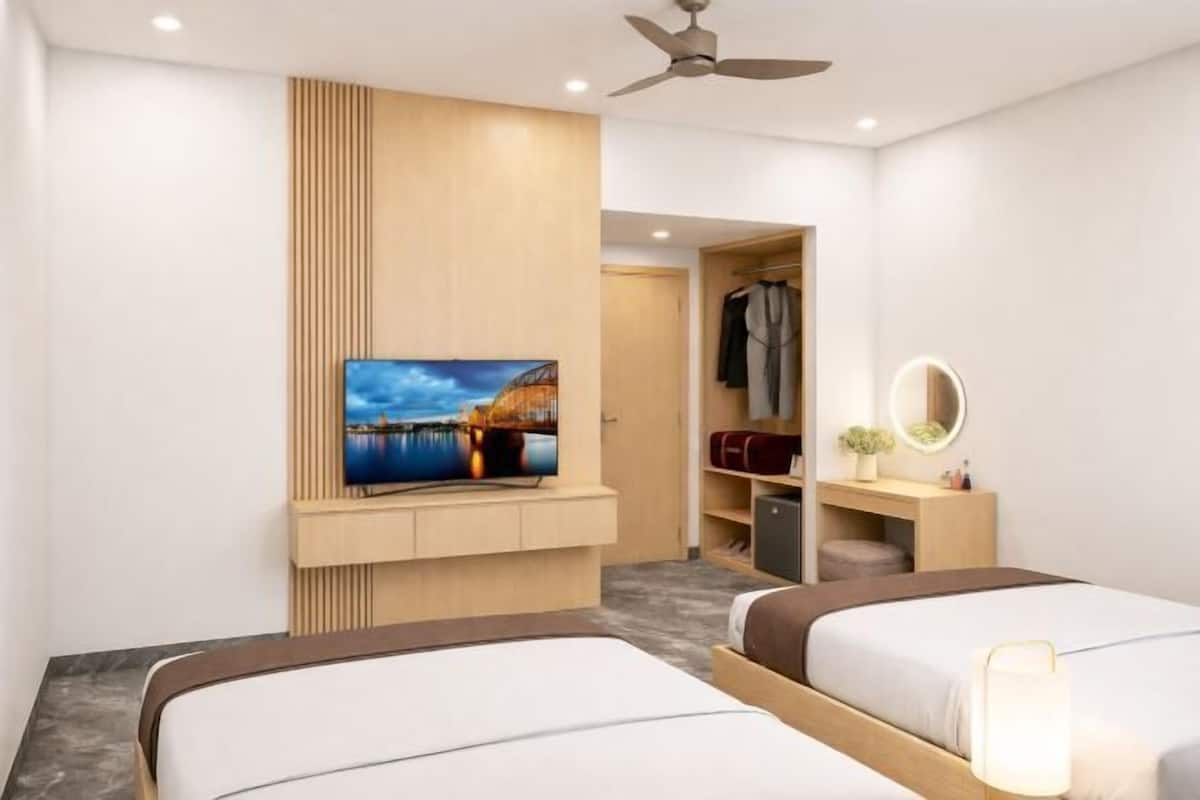 Une chambre d’hôtel avec deux lits, un téléviseur fixé au mur, un ventilateur de plafond et une armoire.