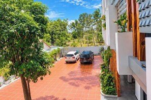 A residential area with a paved driveway, two parked cars, and a tree.
