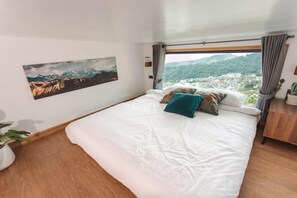 Een slaapkamer met een groot bed, uitzicht op een stad en bergen, en een houten vloer.
