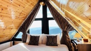 A bedroom with a sloped ceiling, a large window, and a bed with patterned pillows. - Sinsup villa private Mountain View (Mae Suai)