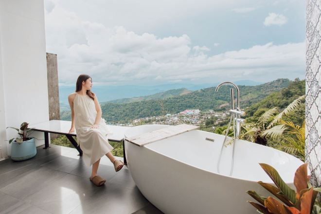 A woman sitting by a bathtub with a view of a mountainous landscape.