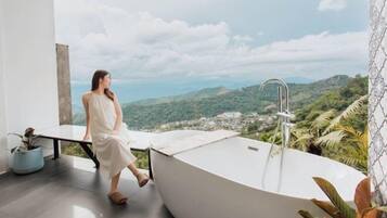 A woman sitting by a bathtub with a view of a mountainous landscape.
