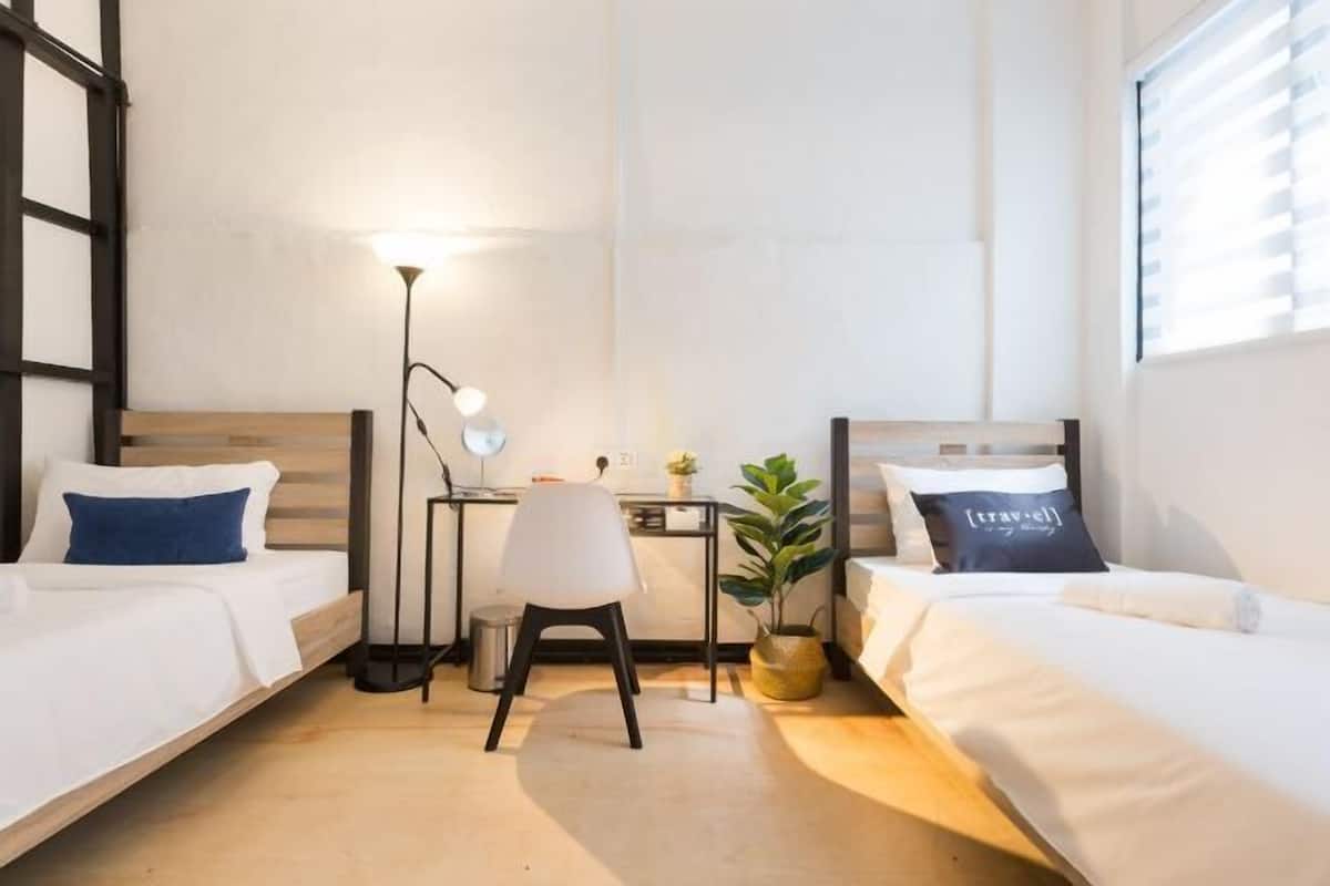 Une chambre avec deux lits simples, un bureau avec une chaise, une lampe et une plante en pot.