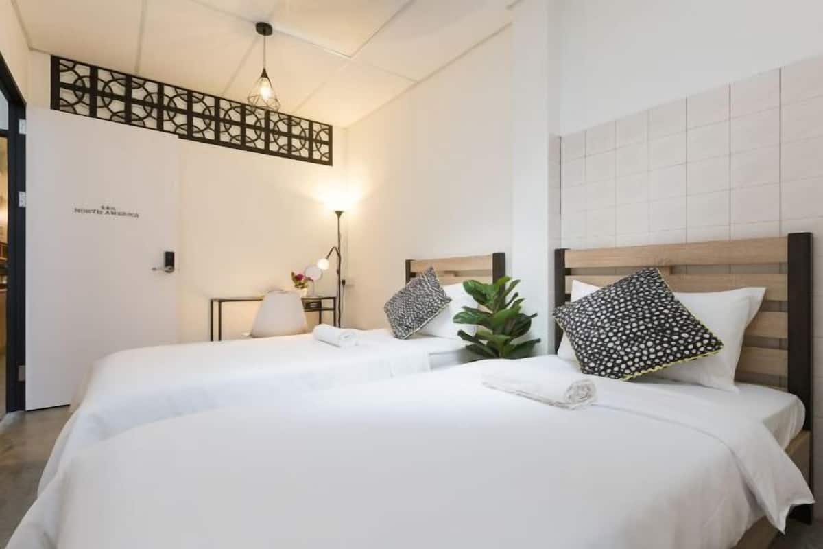 Une chambre d’hôtel avec deux lits, un luminaire fixé au mur, une plante et un panneau décoratif.