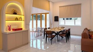A modern dining area with a marble floor, a central table with chairs, and a sofa in the background. - Aesthetic Muji Pool Villa in Ipoh 5BR 24Pax (Tambun)