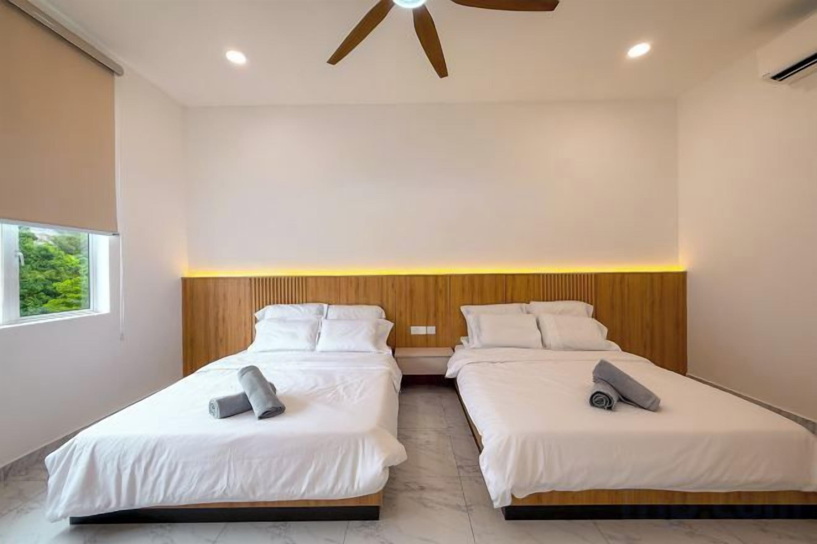 A hotel room with two beds, a ceiling fan, and a window with a view of greenery.
