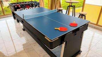 A ping pong table with two paddles, a foosball table, and a bar area with stools.