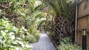 A narrow brick pathway flanked by lush greenery and a wooden fence. - Seaside 1-bed Stay Near Cafes & Attractions (Melbourne)