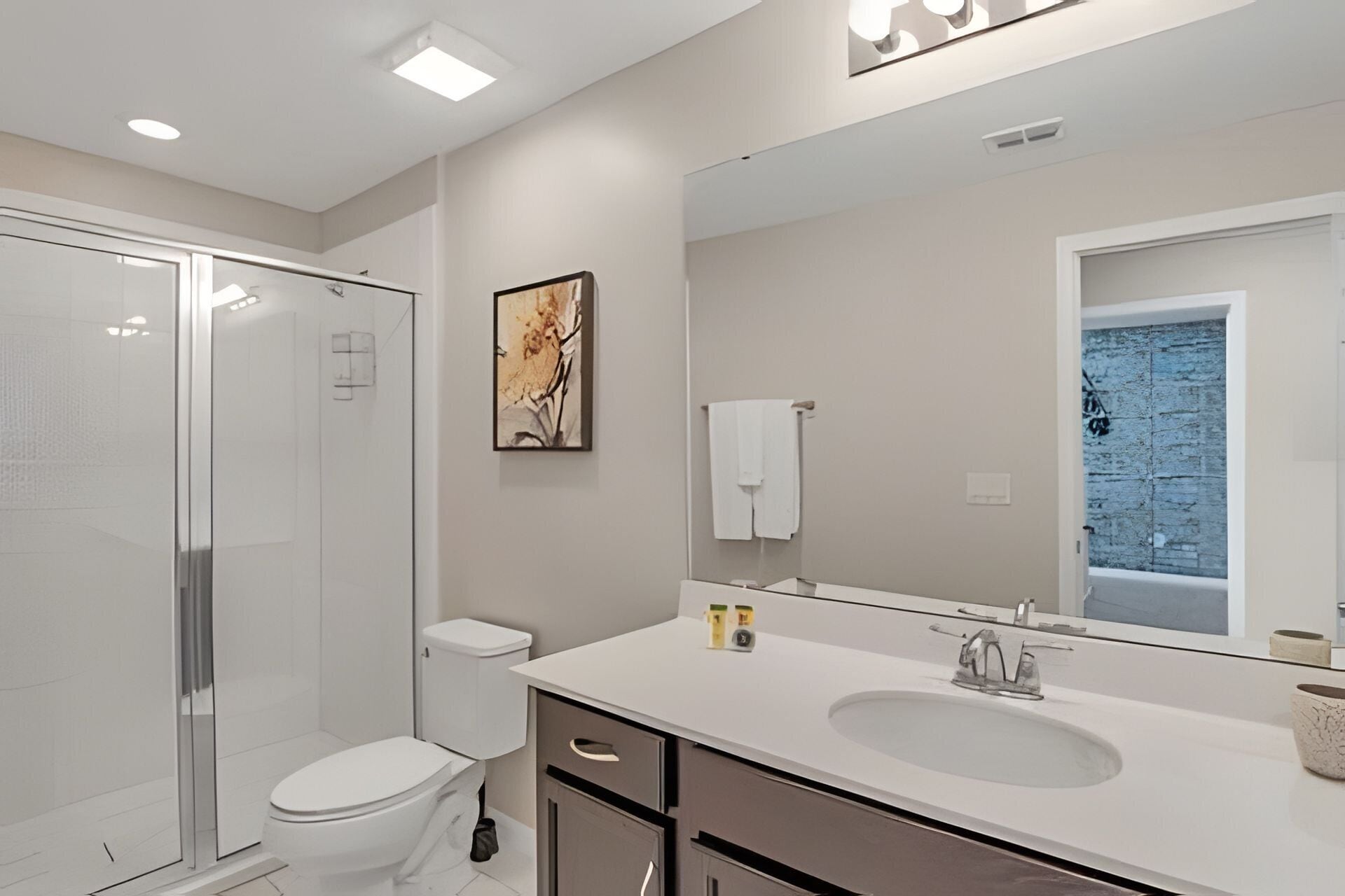 A modern bathroom with a glass shower enclosure, a toilet, a sink with a mirror, and a towel rack.