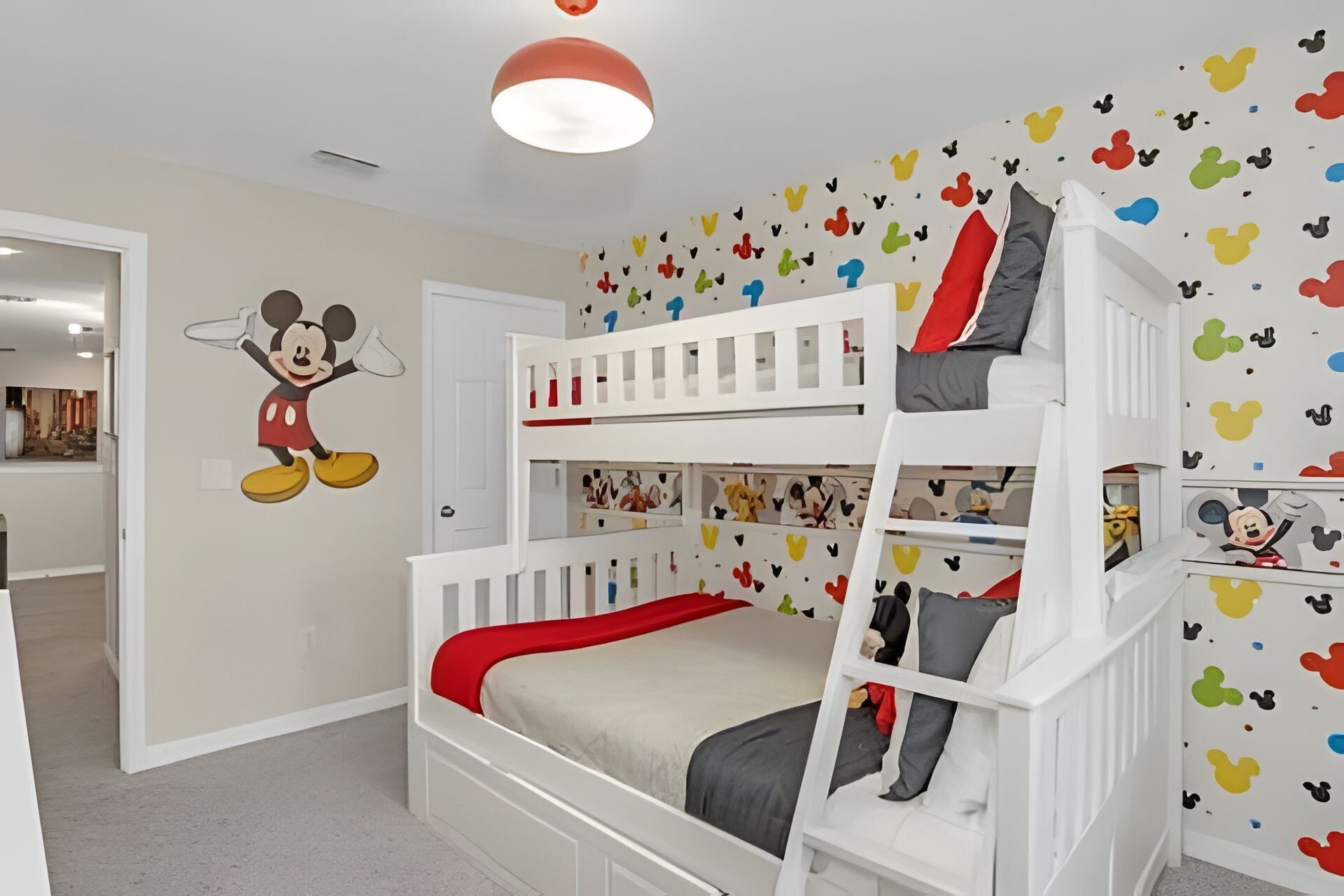 Habitación infantil con literas, un adhesivo de pared de Mickey Mouse y una lámpara de techo.