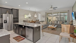 A modern kitchen with a central island, built-in appliances, and a dining area with a sofa and coffee table. - Luxury 5-bed Home With Private Splash Pool (Kissimmee)