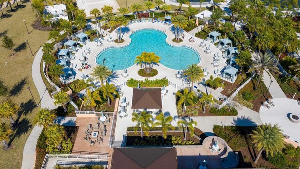 An aerial view of a resort with a central swimming pool, surrounded by lounge areas with umbrellas, palm trees, and a beach area. - Luxury 5-bed Home With Private Splash Pool (Kissimmee)