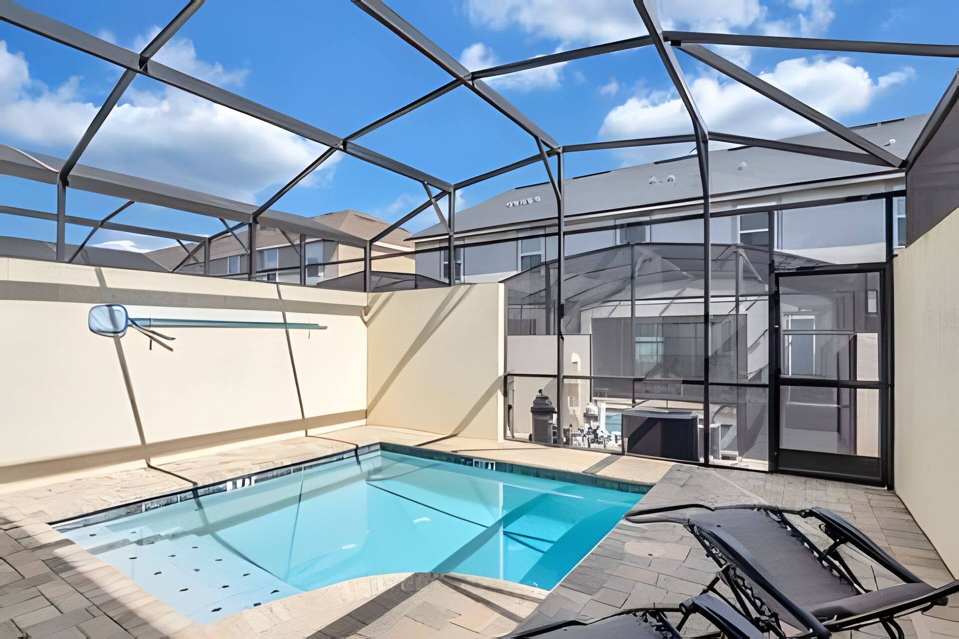A swimming pool with a glass enclosure, lounge chairs, and a view of the surrounding buildings.