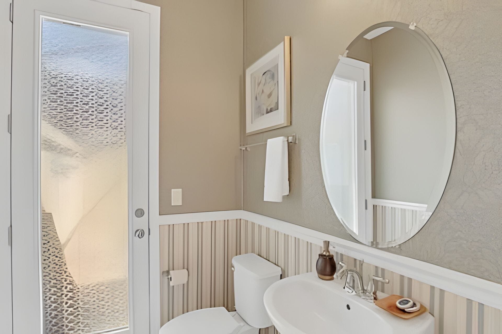 Een badkamer met een witte wastafel, een grote spiegel en een toilet. Er hangt een ingelijst schilderij aan de muur en een handdoek op een rek.