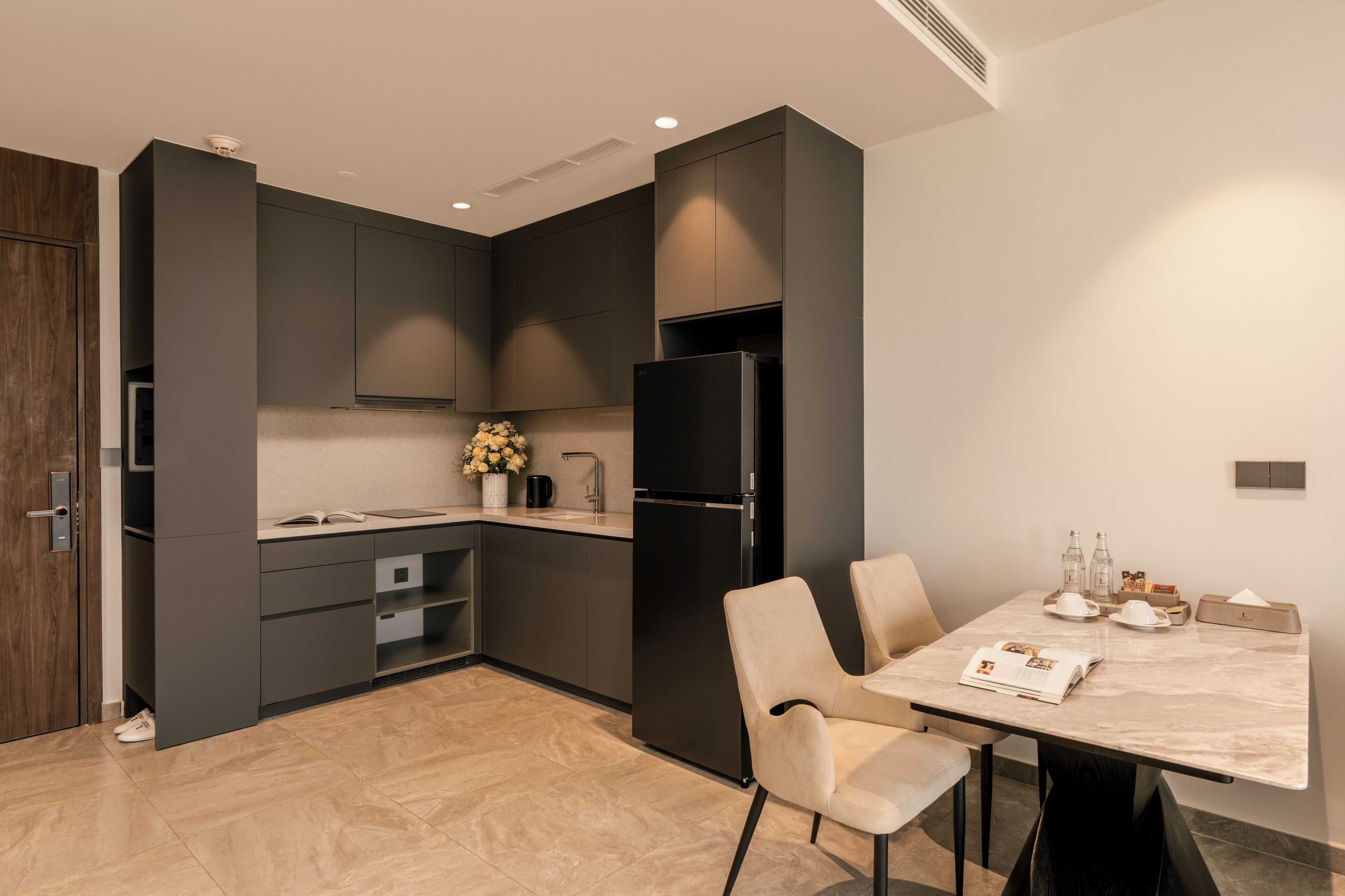 A modern kitchen with dark cabinetry, a black refrigerator, and a dining area with a marble table and chairs.