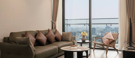A modern living room with a sofa, a round coffee table, a chair, and a view of a cityscape through large windows.