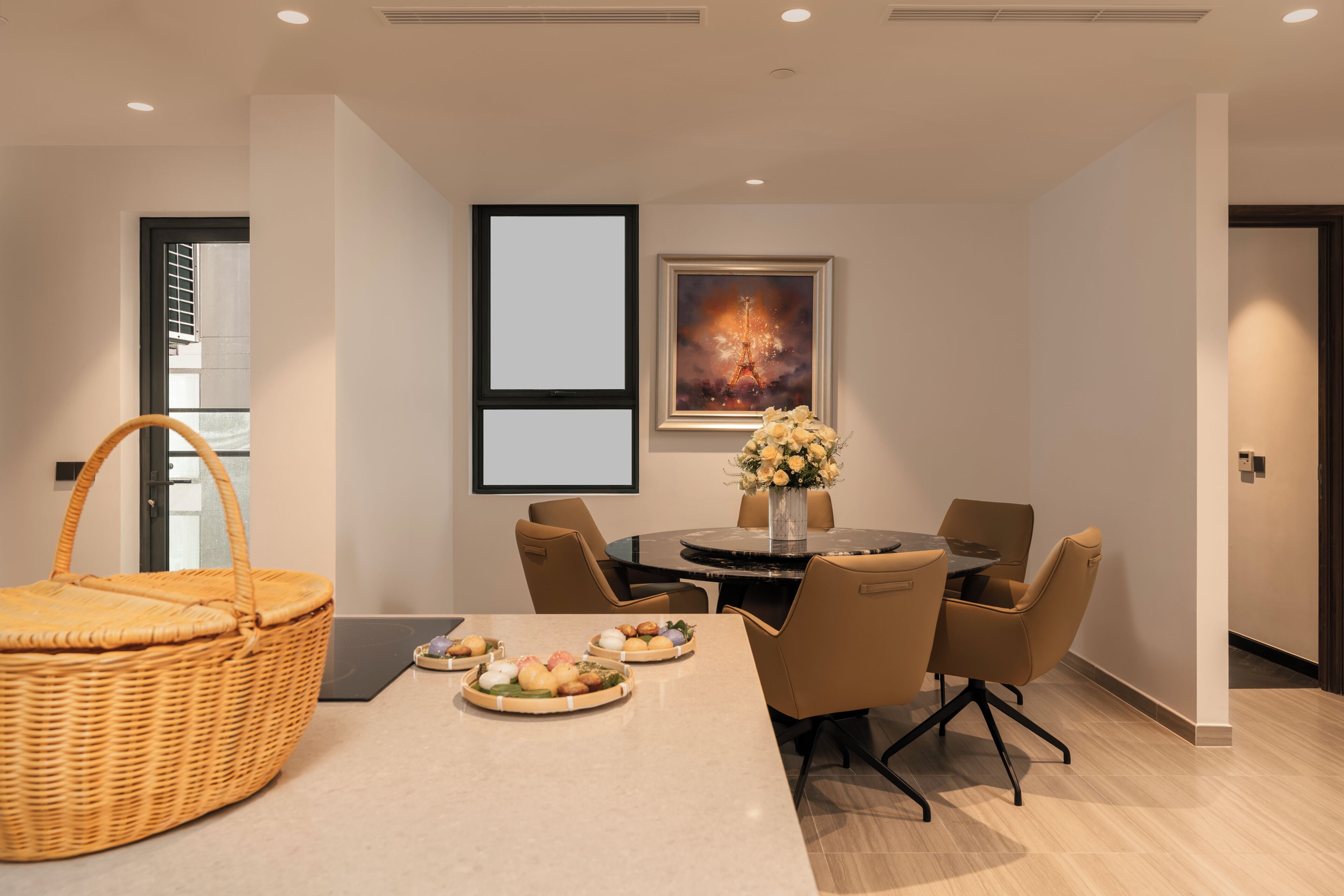 A modern dining area with a round table, chairs, a basket, and a vase with flowers.