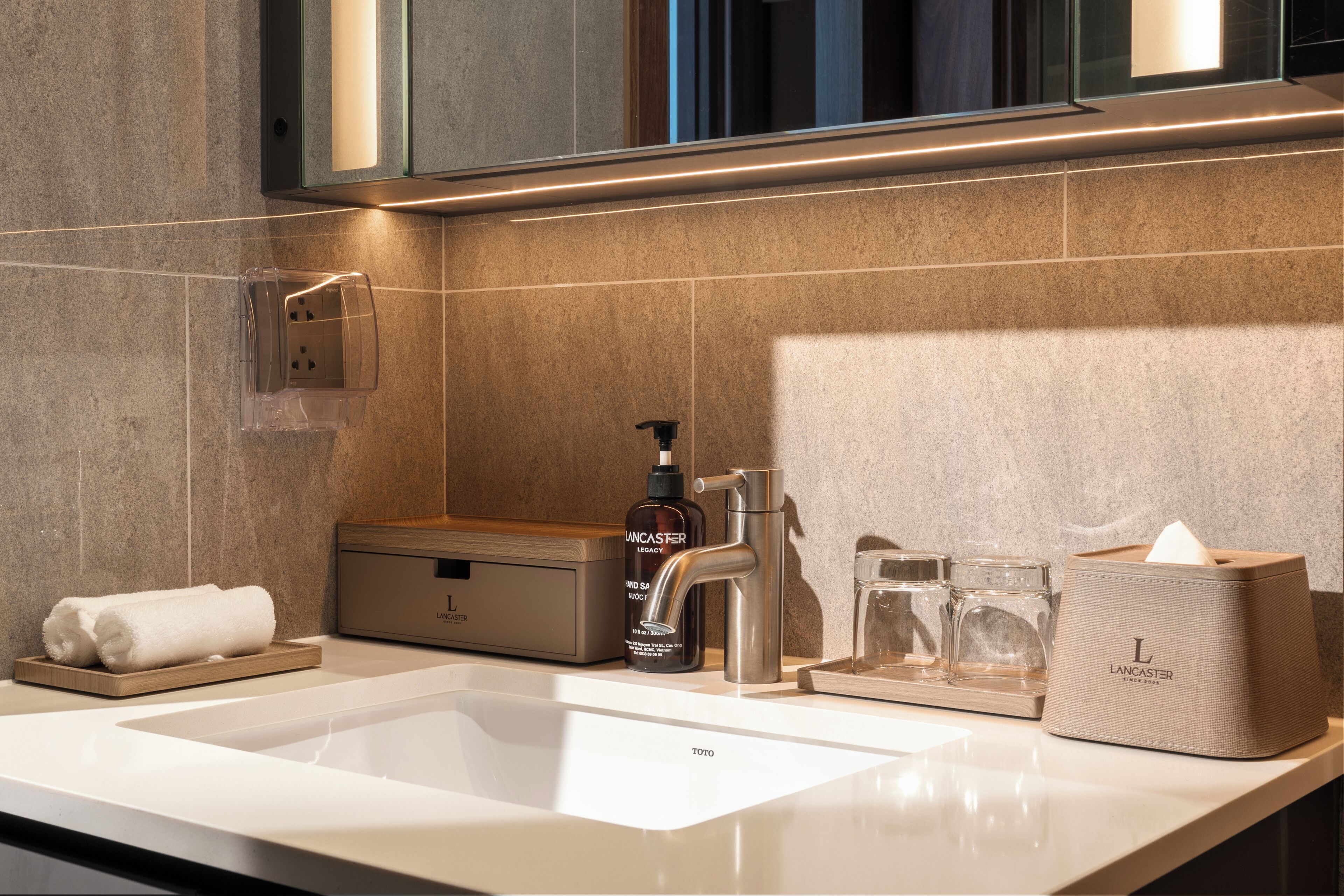 A modern bathroom with a large sink, a mirror, a towel rack, a soap dispenser, and a tissue box.