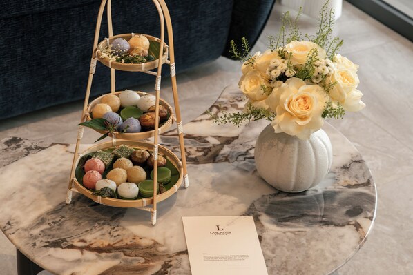 A marble table with a tiered basket of assorted pastries, a vase of flowers, and a business card. - Lancaster Legacy Hotel & Apartments (Ho Chi Minh City)