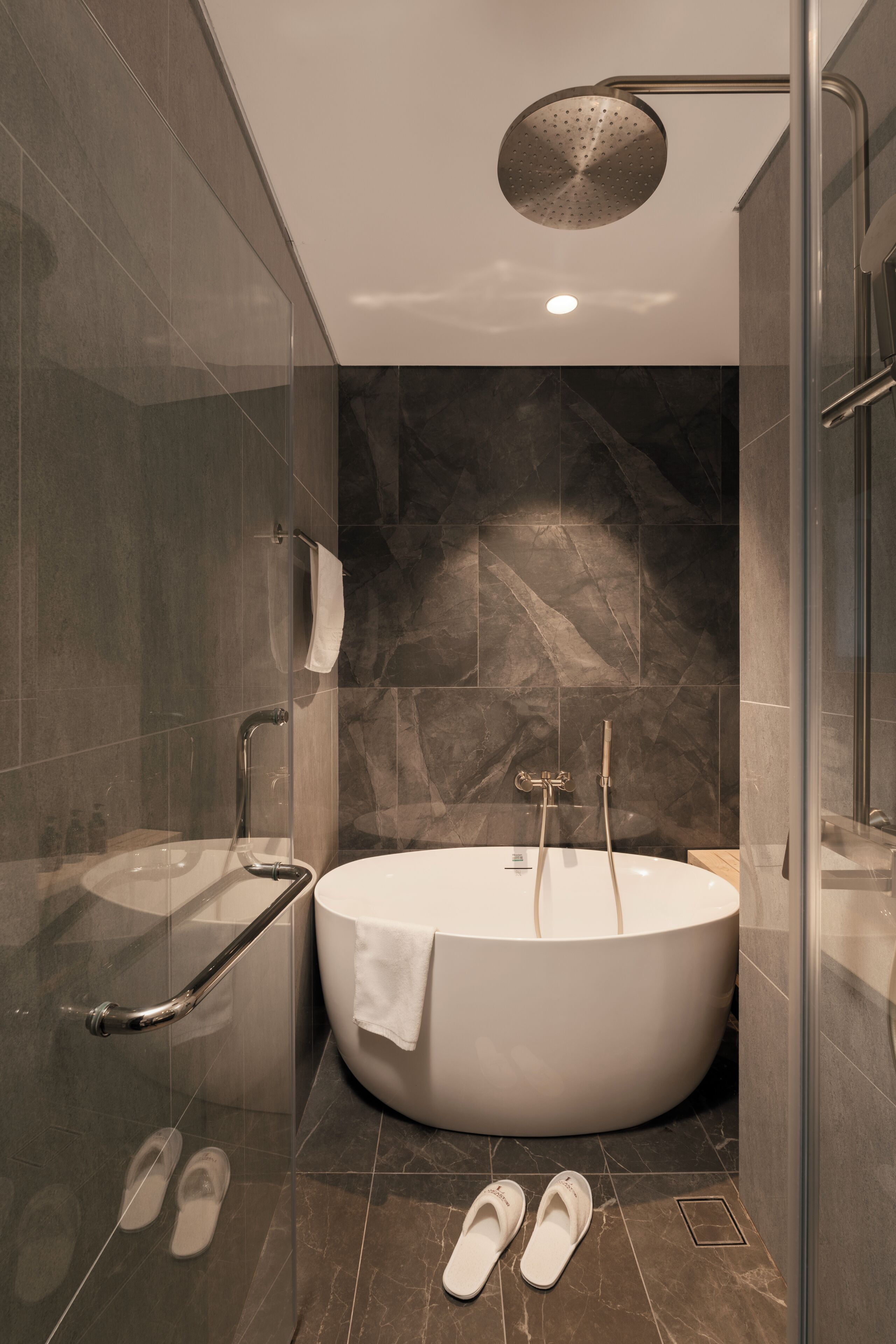 A modern bathroom with a freestanding bathtub, a glass shower enclosure, and a handrail.