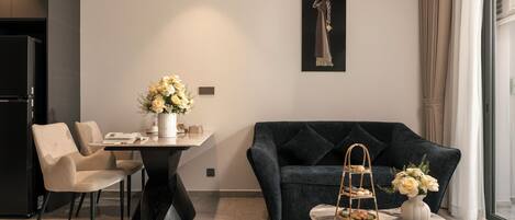 Una sala moderna con un sofá azul oscuro, una mesa de comedor con sillas, una mesita de centro con un jarrón y una cesta, y un cuadro en la pared.