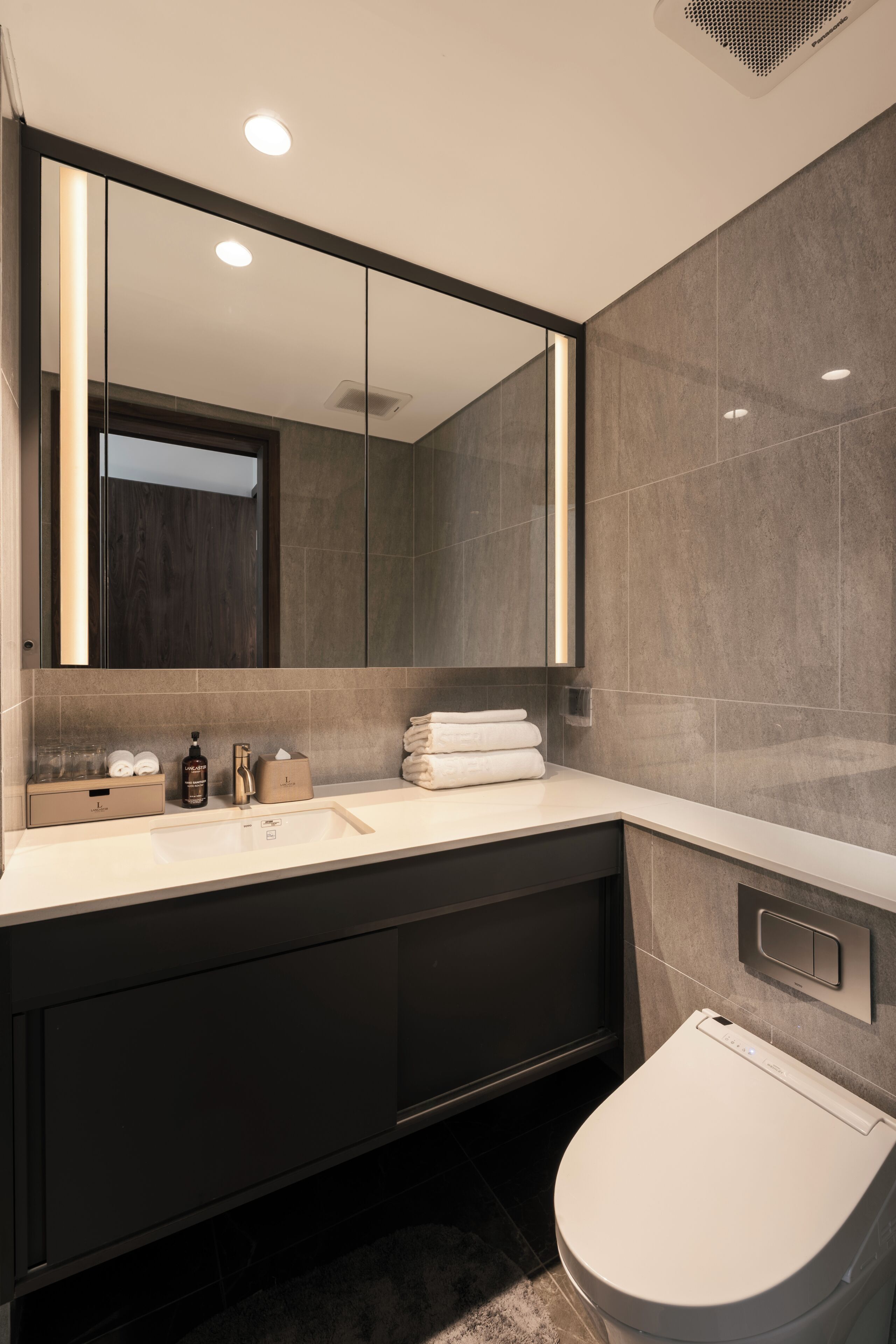 A modern bathroom with a large mirror, a toilet, and a vanity with a sink and storage.