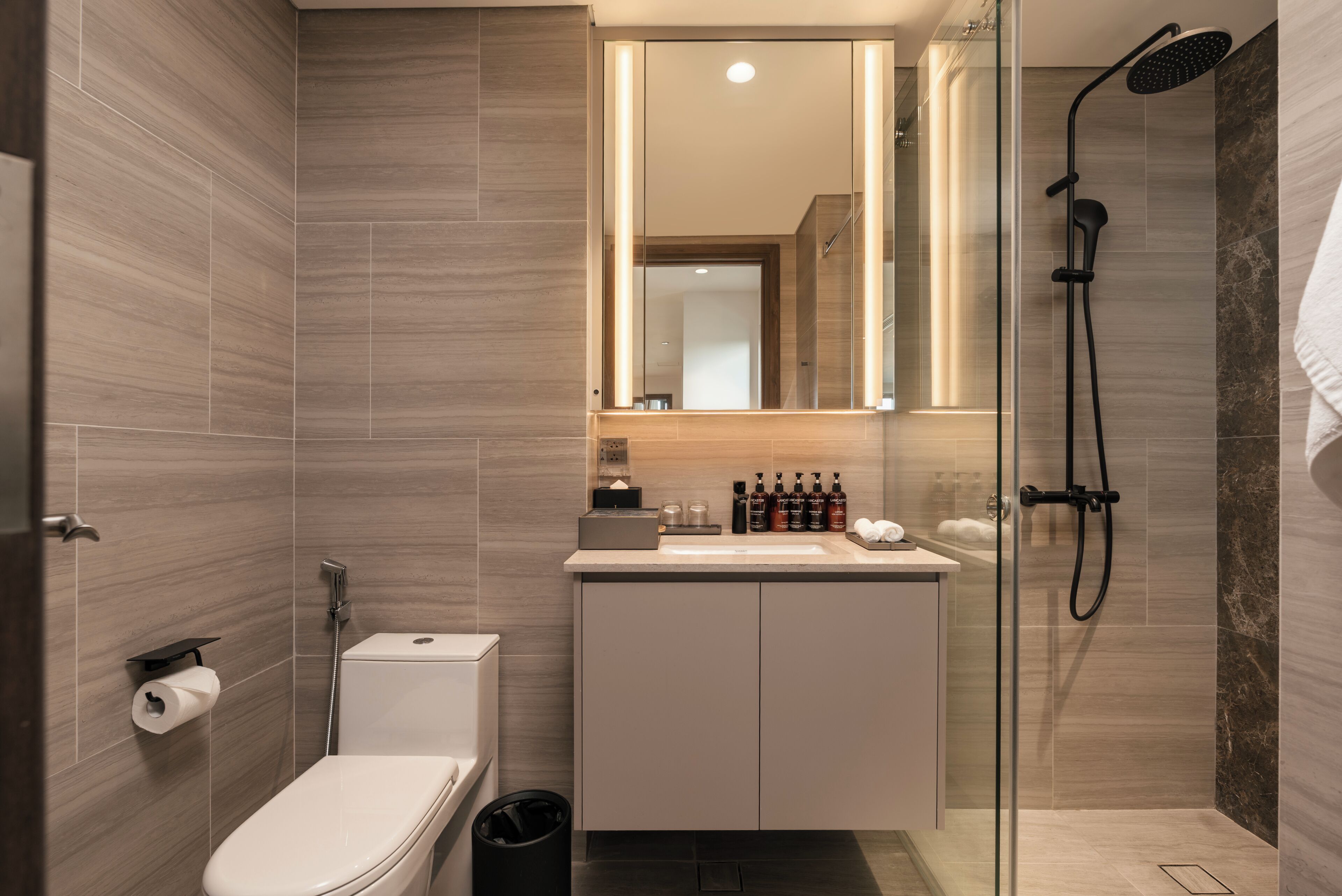 A modern bathroom with a toilet, sink, mirror, and shower.