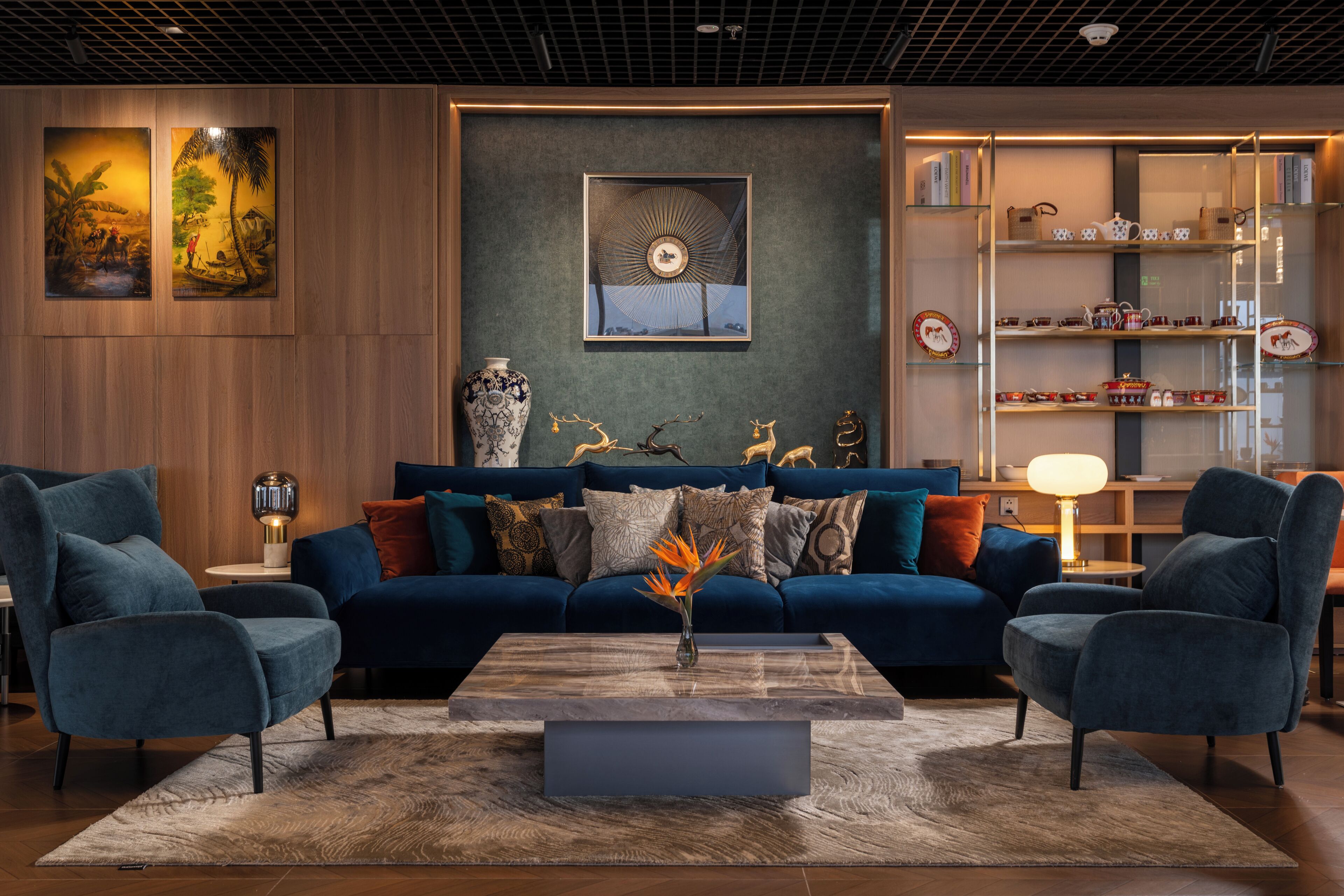 A modern living room with a blue sofa, two armchairs, a coffee table, and a bookshelf with decorative items.