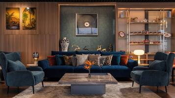 A modern living room with a blue sofa, two armchairs, a coffee table, and a bookshelf with decorative items.