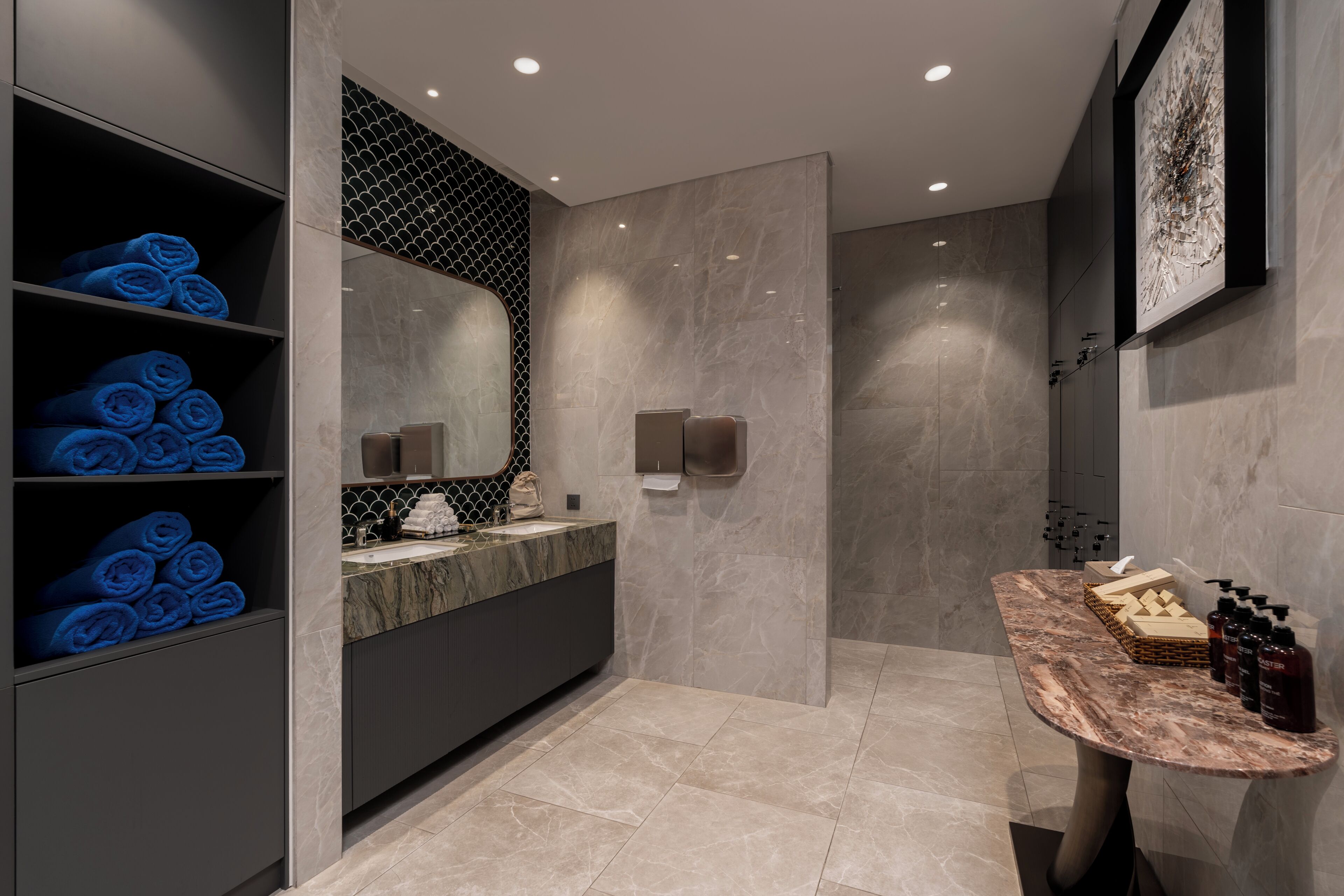 Une salle de bain moderne avec des carreaux de marbre, une étagère intégrée où sont rangées des serviettes bleues, un meuble-lavabo avec un plan de travail en marbre et un espace douche.