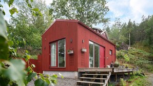Une cabane en bois rouge avec de grandes fenêtres, une terrasse en bois et un jardin.