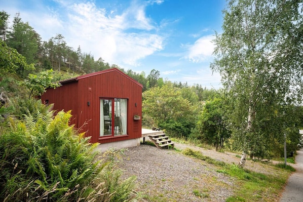 A red wooden cabin with a gravel path leading to a wooden staircase.