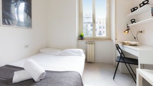 A bedroom with a bed, a desk, and a window.