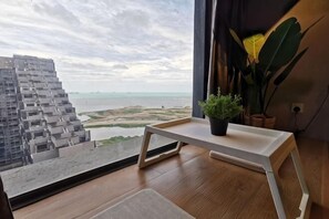 A room with a view of a distant building and water, a small table with a plant, and a potted plant on the windowsill.