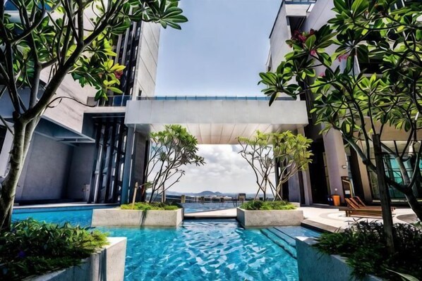 A modern hotel pool area with a clear view of the sea, surrounded by greenery and contemporary architecture.