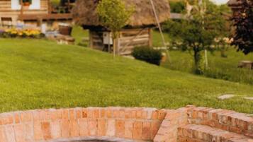 A brick outdoor fireplace surrounded by a grassy area with a thatched-roof structure in the background.